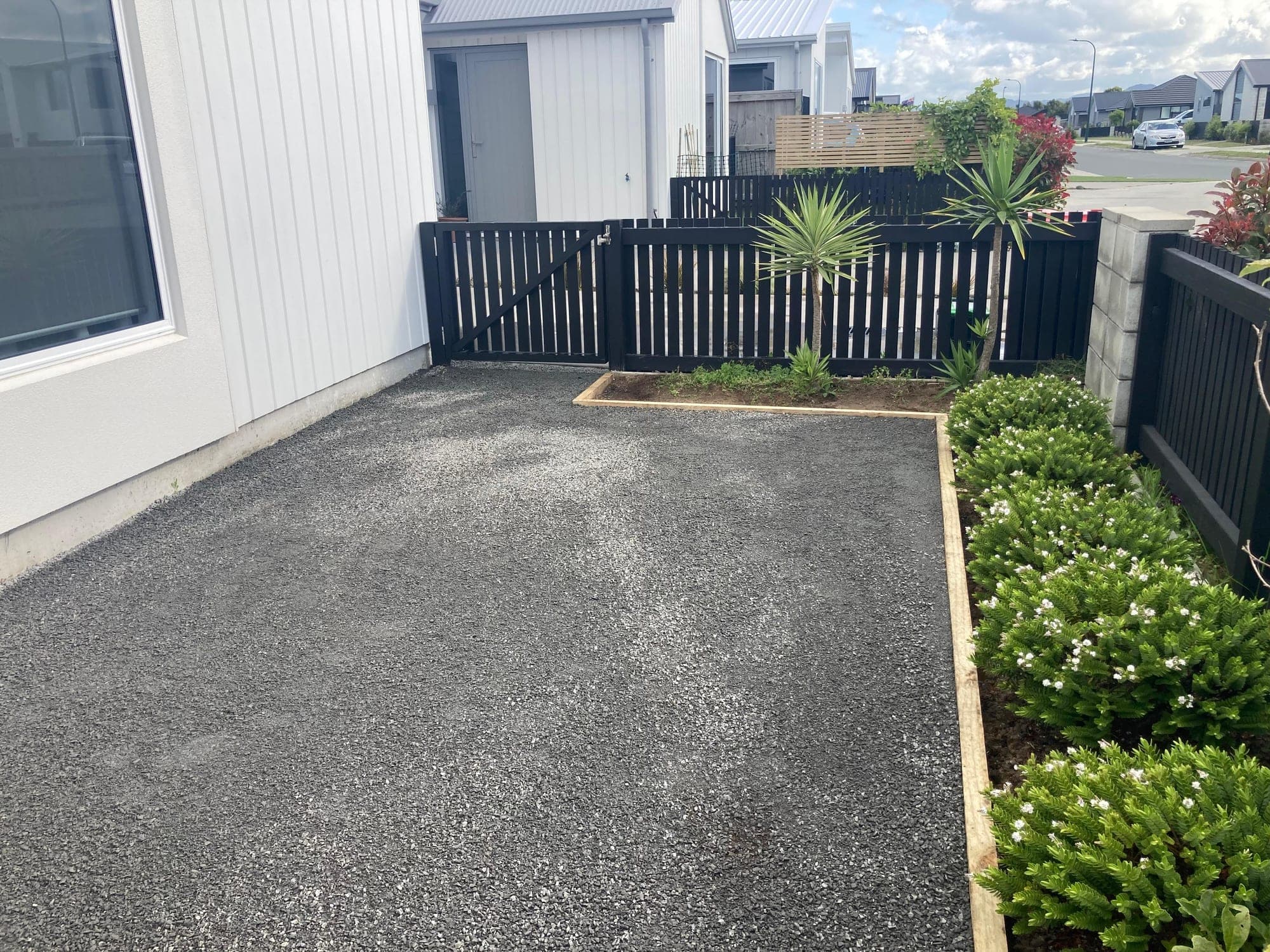 Front yard prepared with a compacted basecourse, timber edging and a planted border beside a black slat fence