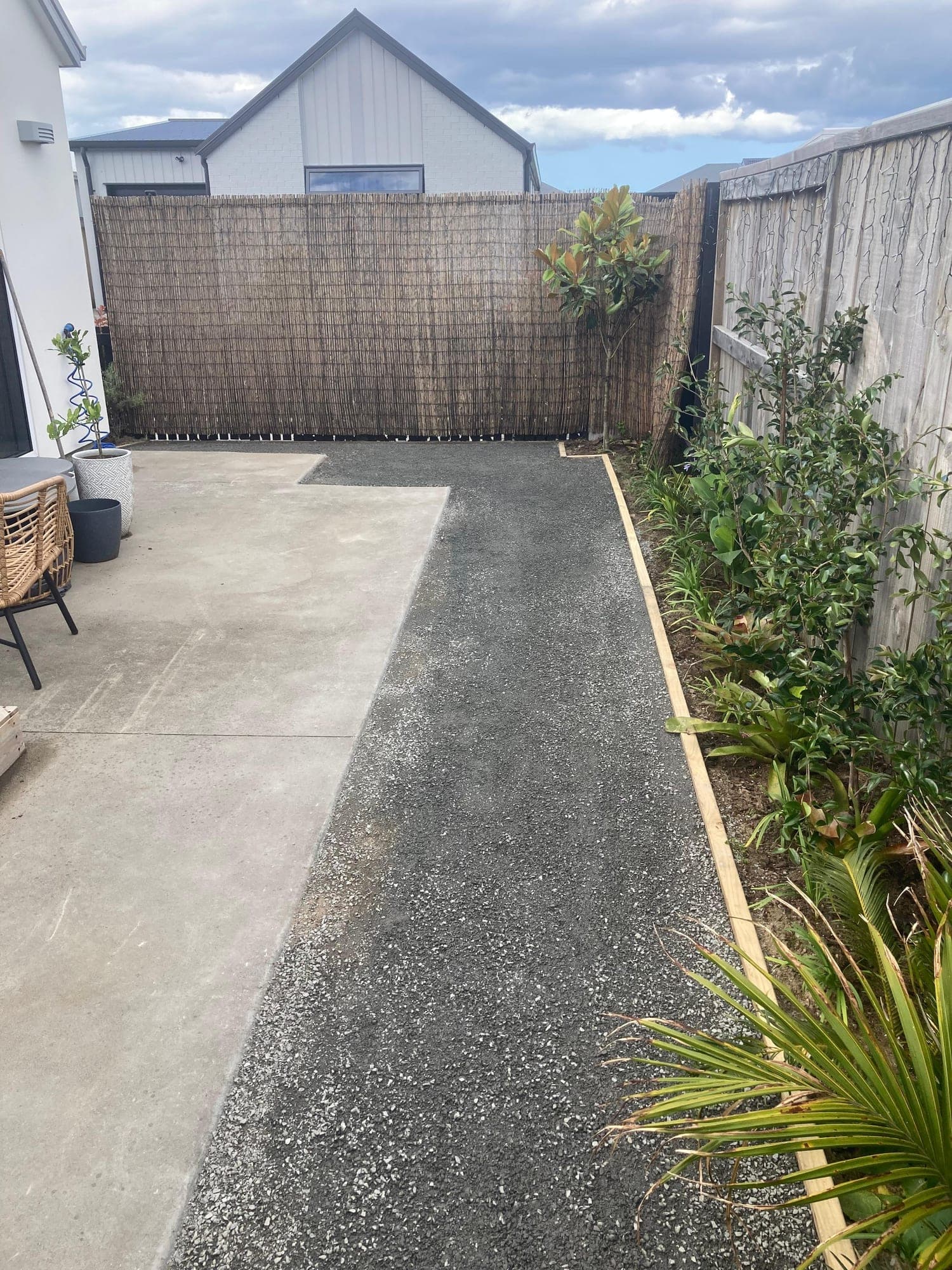 Compacted basecourse beside a concrete patio, edged in timber against a garden bed