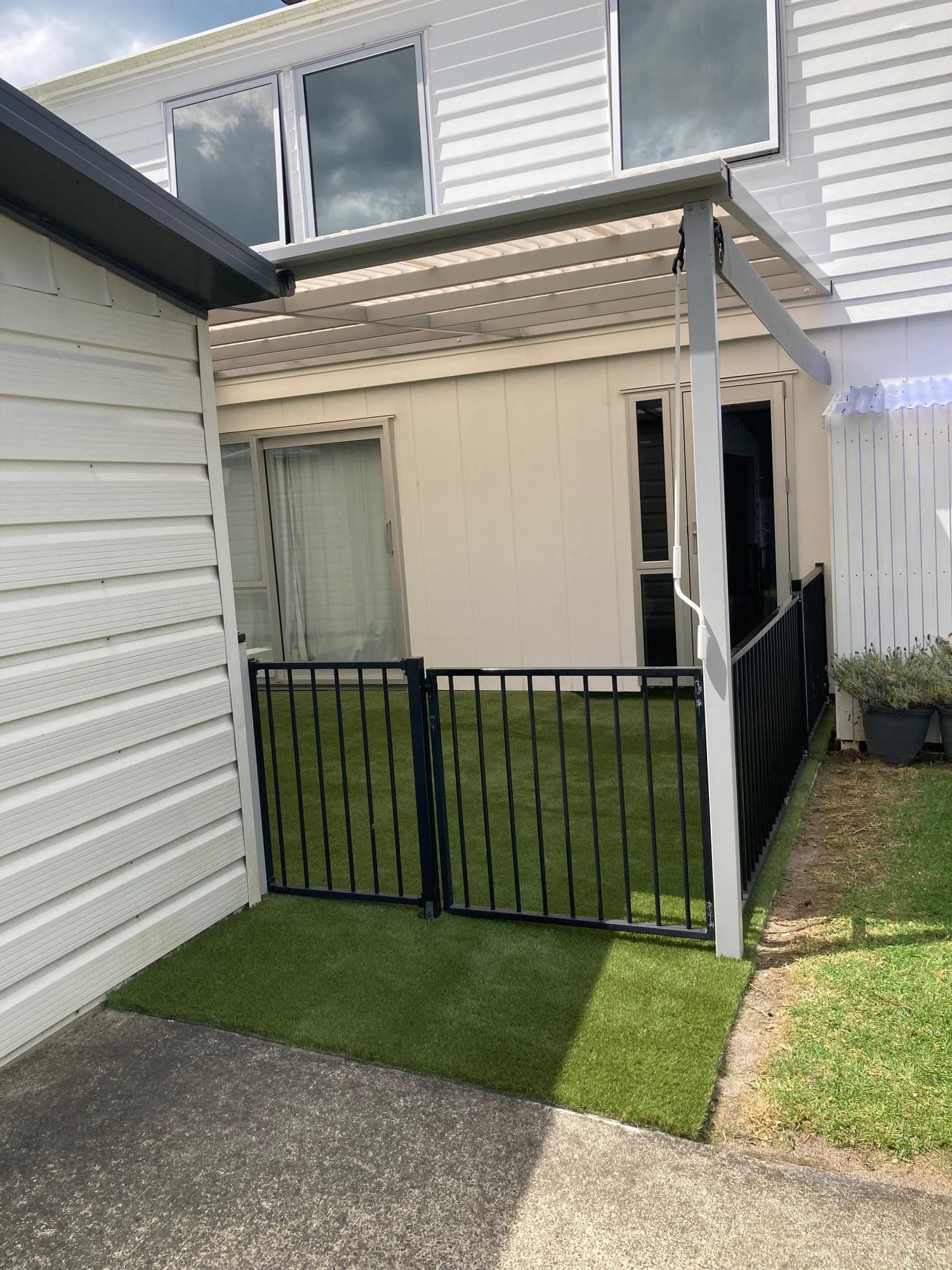 Black pool fence gate opening onto artificial turf in a sheltered courtyard